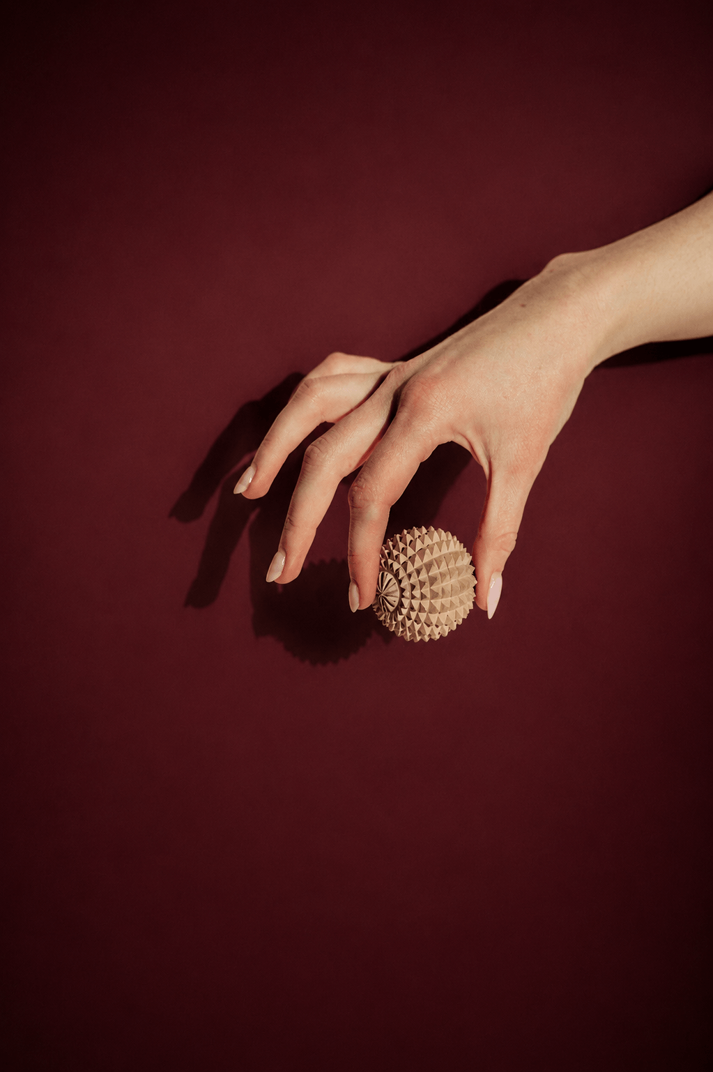 Hand holding a beige textured sensory stress relief ball with a geometric pattern on a dark red background
