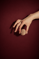 Hand holding a beige textured sensory stress relief ball with a geometric pattern on a dark red background